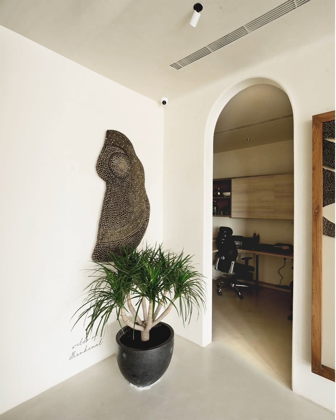 Cream Carrara-finished walls and arched doorway with a dark wall sculpture and plant, opening to a home office Cream Carrara-finished walls and arched doorway with a dark wall sculpture and plant, opening to a home office